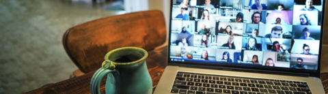 Green ceramic mug beside a laptop displaying a video conference with multiple participants.