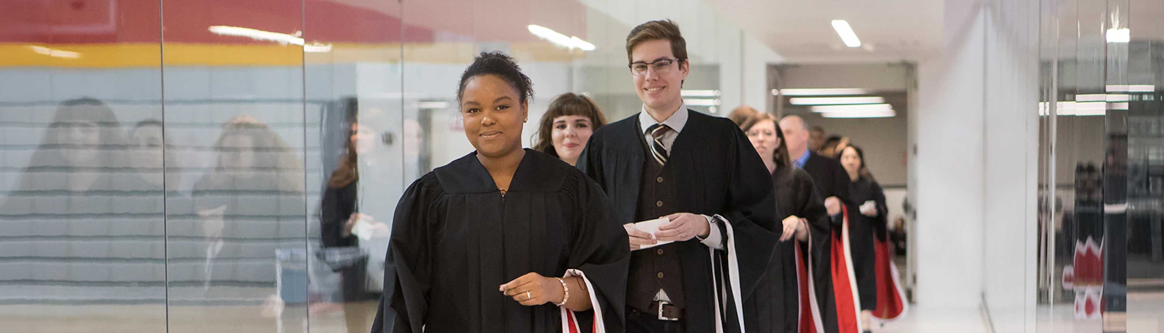 University of Guelph graduates in black gowns walking through a hallway during a graduation ceremony.