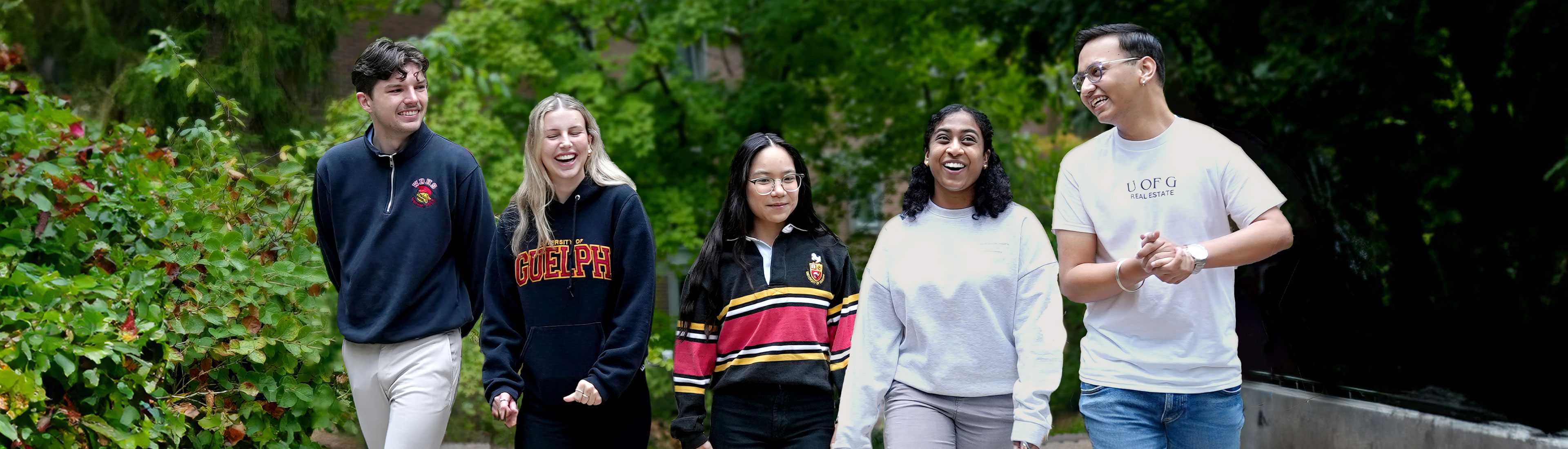 Five University of Guelph students walk together outdoors, smiling and laughing, wearing University of Guelph apparel and casual clothing against a backdrop of green trees. Have they separated out the card image from the banner for stories yet?