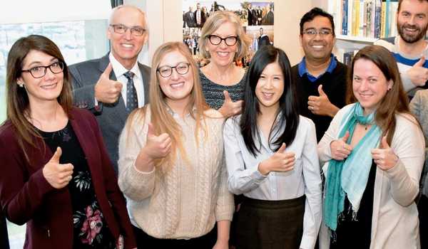 Group of diverse professionals smiling and giving a thumbs-up in an office environment, celebrating a shared success.